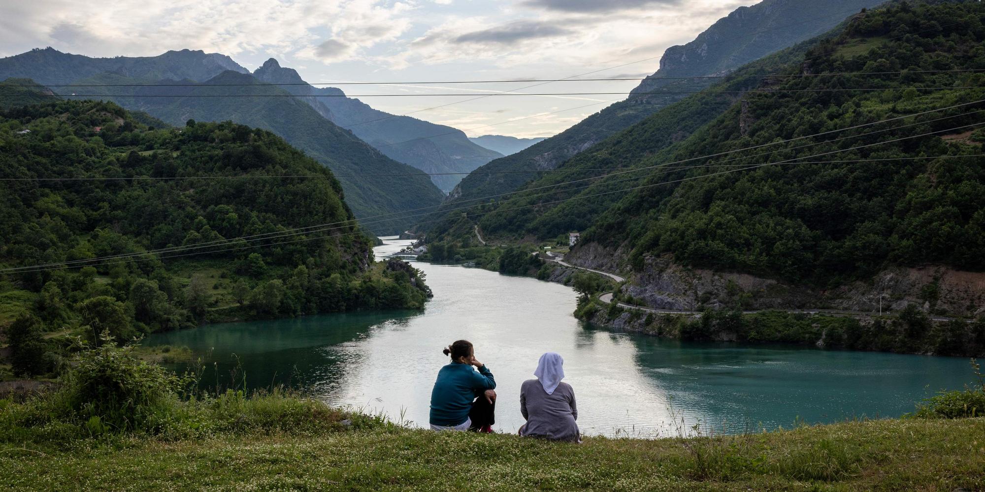 Two women sit on a meadow and look down at the river.