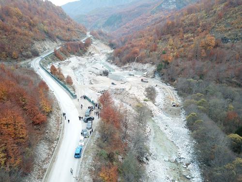 Power station construction site on the Valbona with access road, vehicles and people.